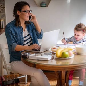 Photo of a little girl who found a way to entertain herself while mom is working on a computer at their dining table